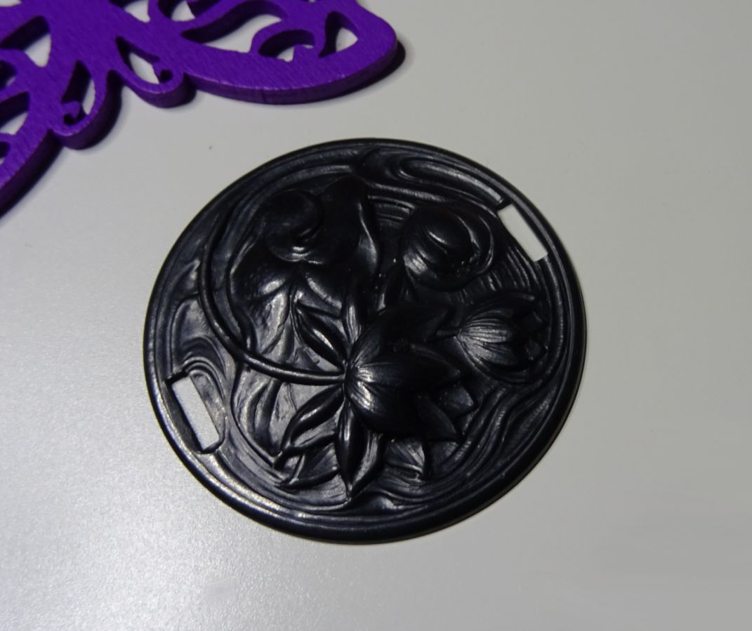 Medalhão de lírio de água em relevo de metal preto com laços laterais 