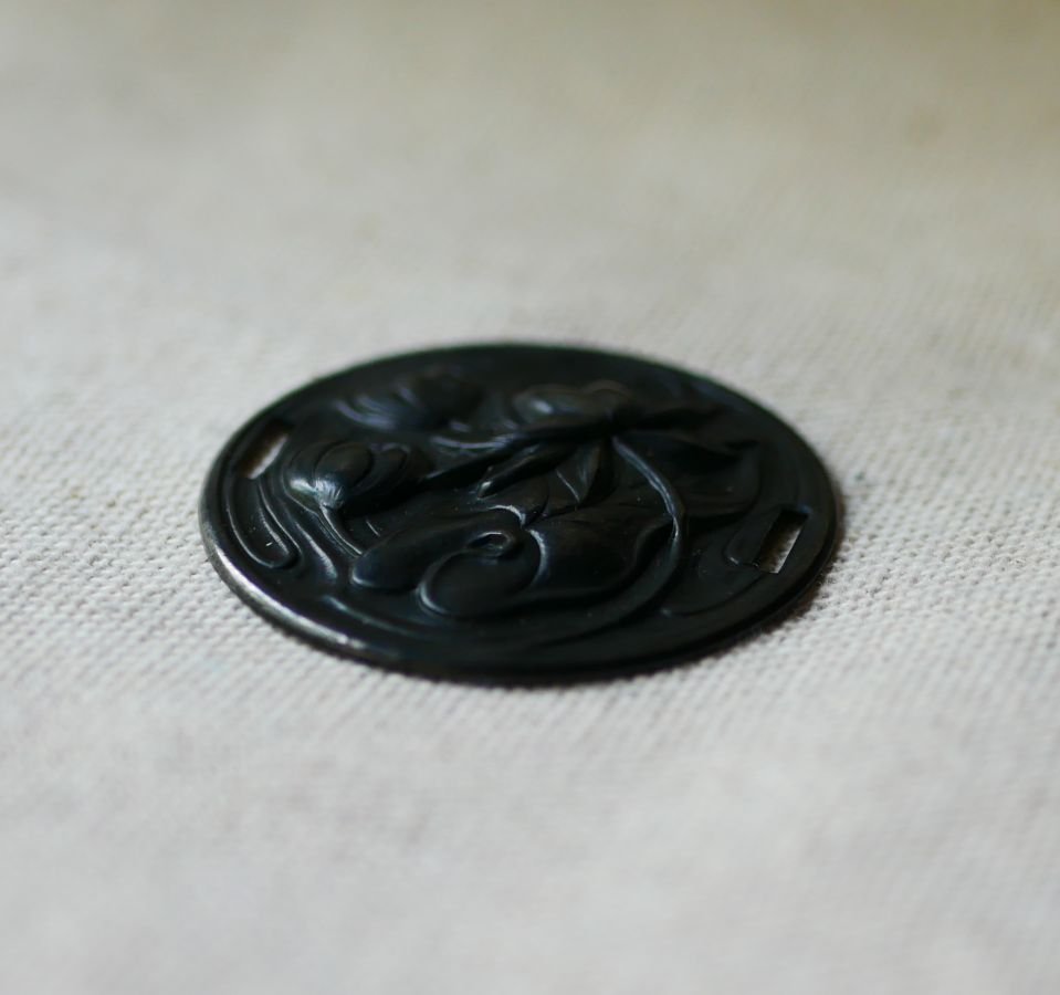 Medalhão de lírio de água em relevo de metal preto com laços laterais 