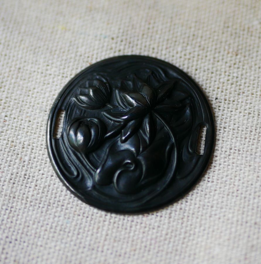 Medalhão de lírio de água em relevo de metal preto com laços laterais 